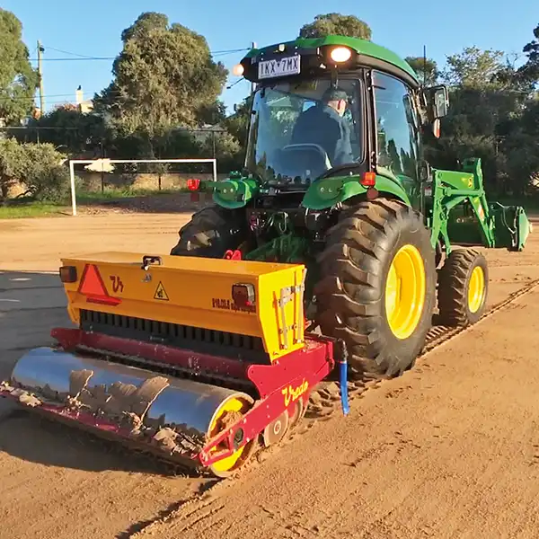 Large tractor pulling roller compacter over soil.